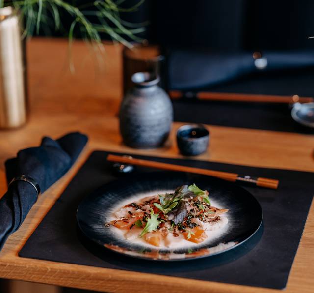 Sashimi in heller Soße im Sushi auf Tellern am Holztisch mit Blumen im Seerestaurant Mizumi